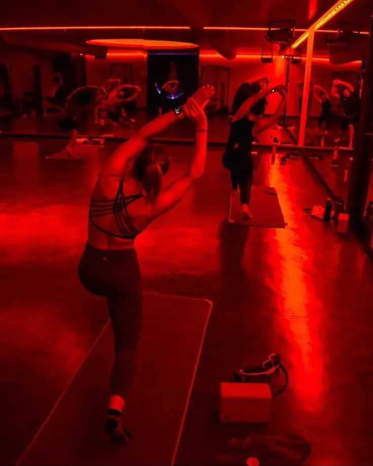 A Red Light X Yoga class stretching in a studio glowing with deep red light